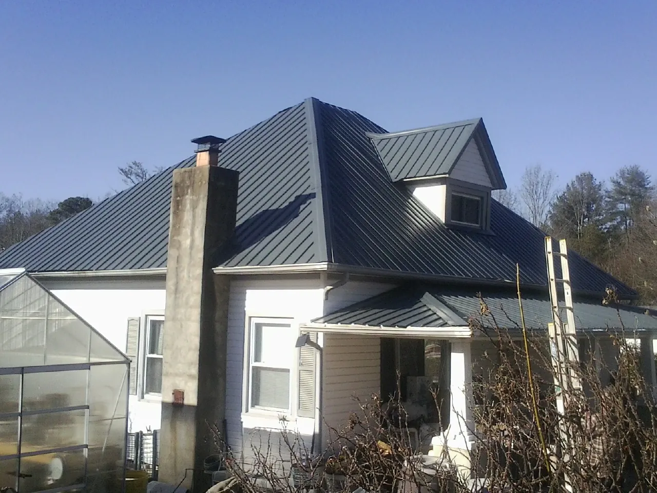 Dark blue standing seam metal roof on a white farmhouse with dormer — Slate & Tile Roof Repair by Roofing Brothers in Hopkinton