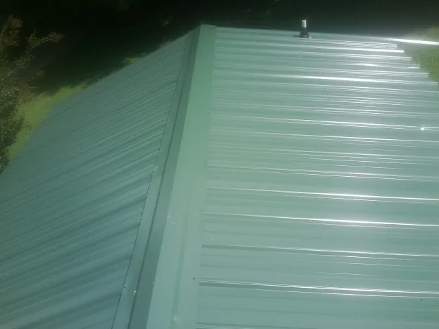 New green metal panels meeting at the ridge of a roof — Flat Roof Repair work by our crew in Hopkinton