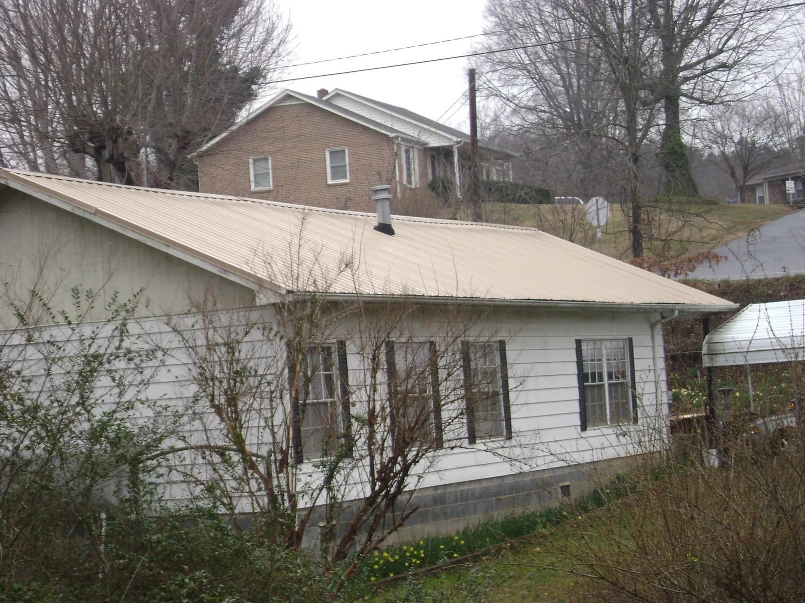 Tan metal roof on a white sided house set into a hillside — Commercial Roofing by Roofing Brothers in Hopkinton